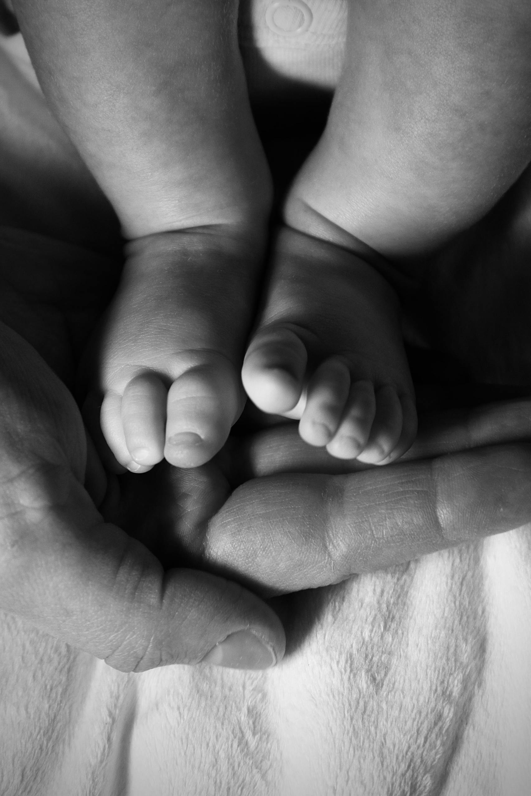 Black and white image of a baby's feet gently held in adult hands.
